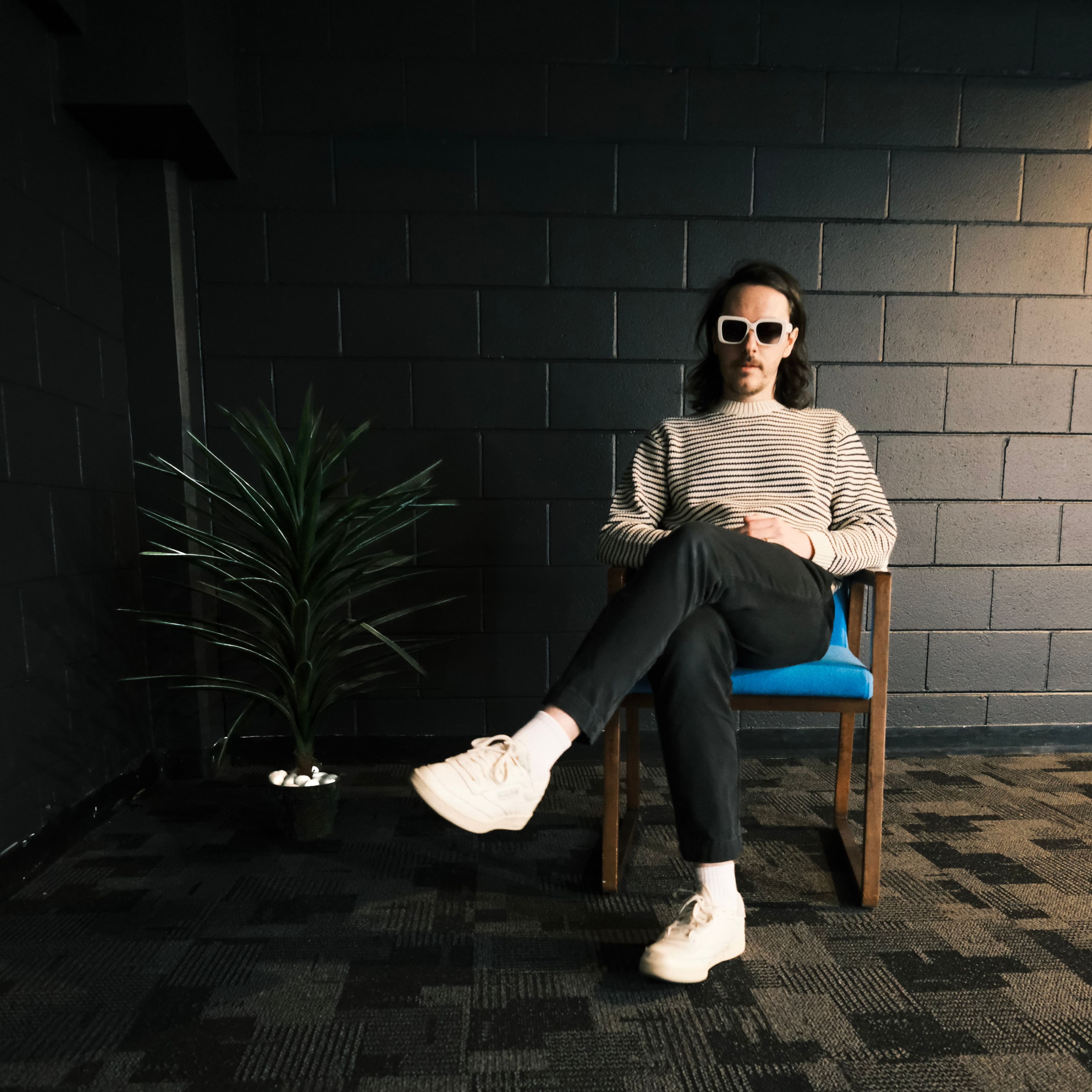 Steve Stout in sunglasses sitting in a chair in a carpeted hallway next to a plant.